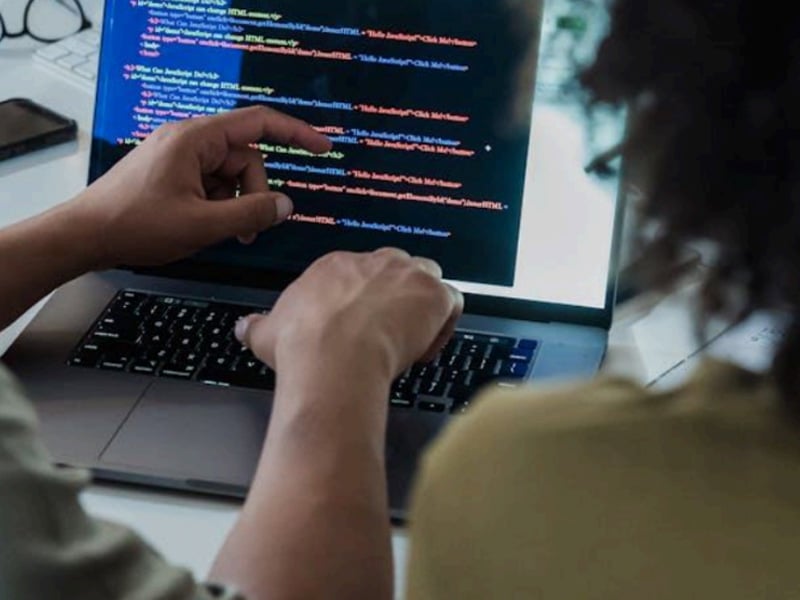 Developers collaborating on HTML and JavaScript code on a laptop screen