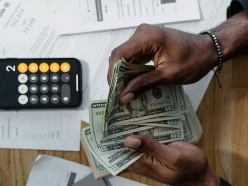 Person managing business finances and counting cash with a smartphone calculator nearby